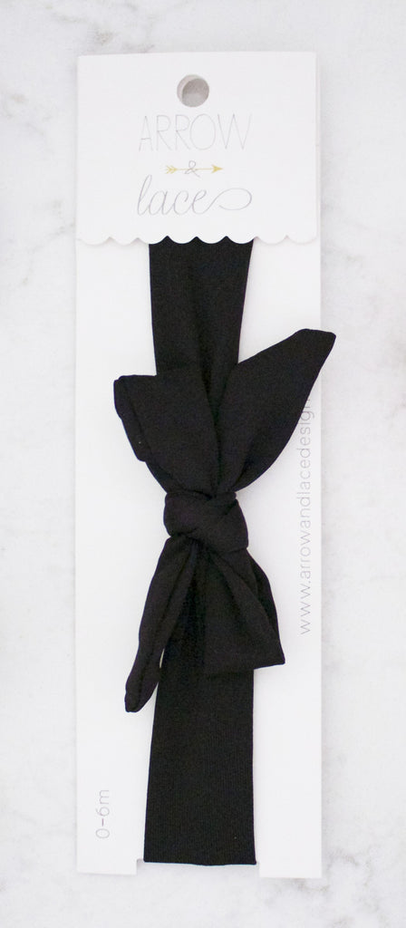 Black hair tie with a knot on a white card with 'Arrow and Lace' branding.