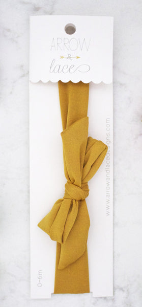 Mustard yellow headband on a white card with visible branding