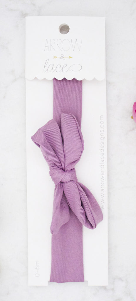 Purple hair bow on a white background with a brand label.